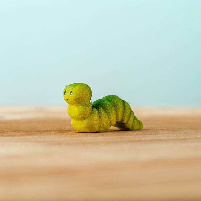Green caterpillar toy on a wooden surface with a light blue background