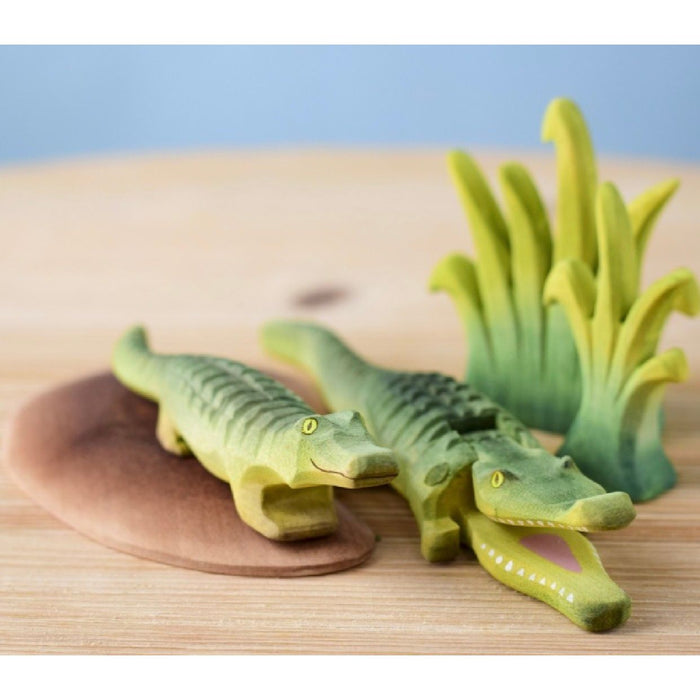 Set of green alligator toys on a wooden surface with a blue background