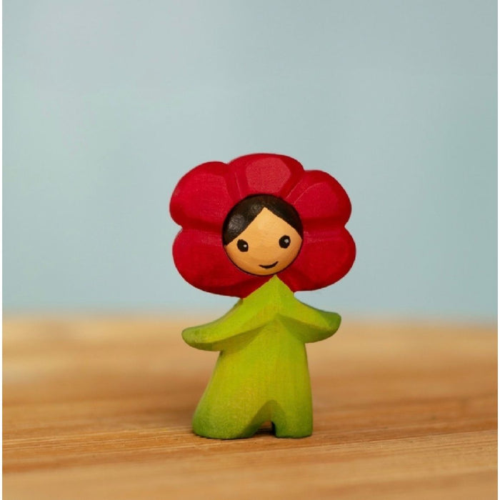 Figurine with red flower head and green body on a wooden surface with light blue background