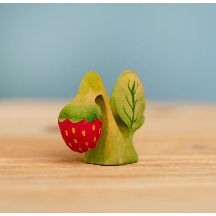 Wooden toy figure of a snail with a strawberry shell on a wooden surface