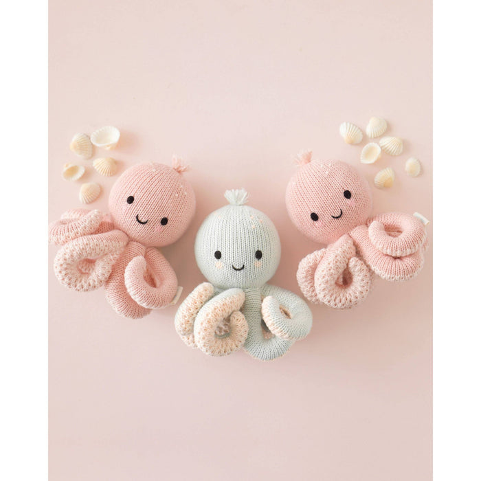 Two pink and one blue knitted octopus toys on a light pink background with small white flowers.