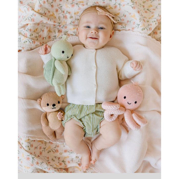 Baby lying on a floral blanket with three soft toys