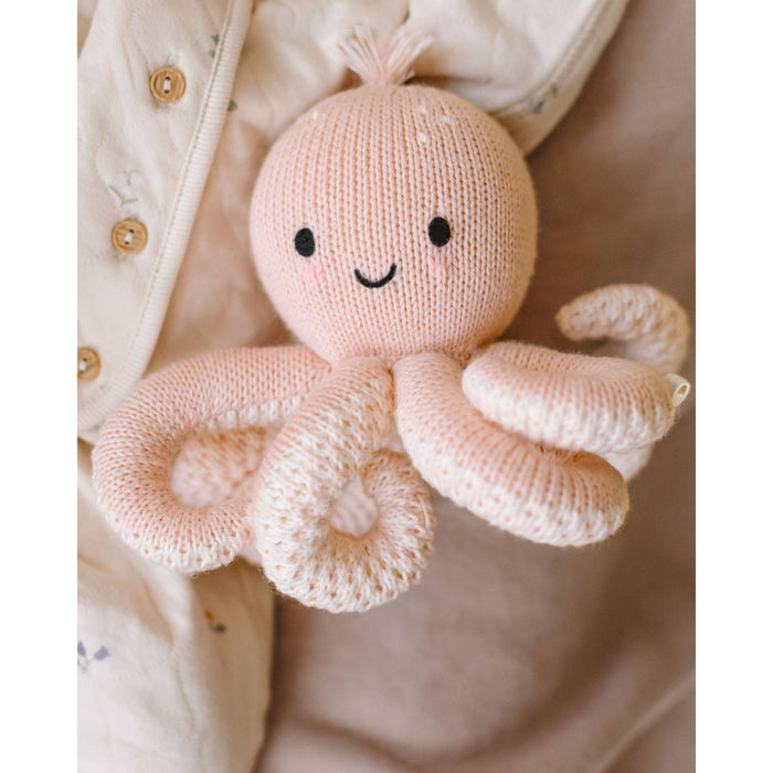 Knitted octopus toy with a smiling face held against a neutral background