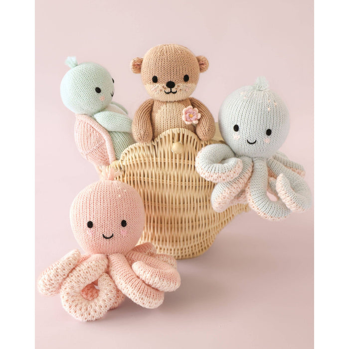 Knitted toys including a bear, octopus, and sea turtle in a wicker basket on a pink background