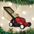 A red and black lawn mower ornament hangs from a Christmas tree, surrounded by green branches and glowing white lights in the background.