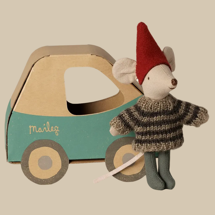 A Maileg toy mouse doll wearing a red felt gnome hat and a brown and beige striped knit sweater, standing next to a cardboard car with a teal lower section and the brand name 'maileg' printed on it.
